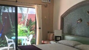 A hotel room with a bed, a small table, and a chair near a sliding glass door leading to an outdoor area with plants. - summerplace inn      (San Miguel II)