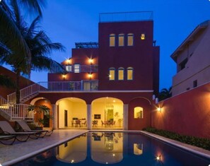 A multi-story hotel with a swimming pool, outdoor seating, and a well-lit entrance.