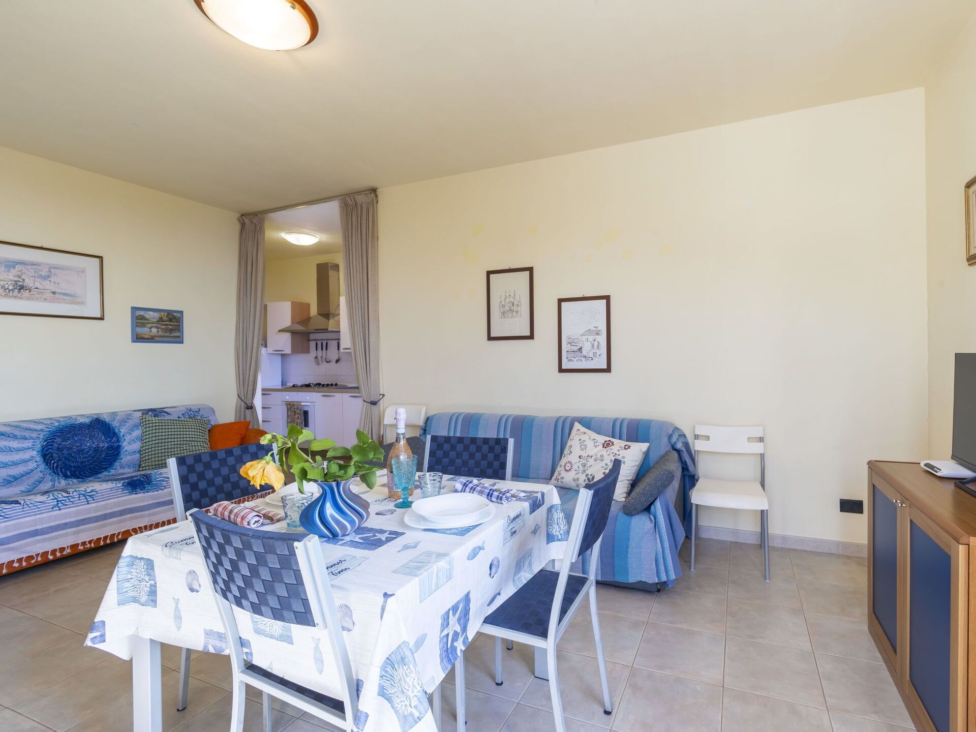 A dining area with a table set for two, a sofa, and a kitchen in the background.