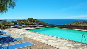 Area piscina con lettini e solarium in pietra, affacciata su un mare cristallino.