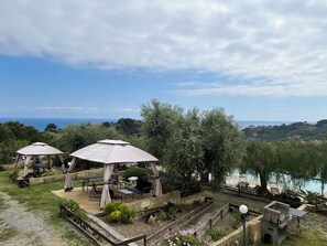 A view of a garden with outdoor seating and a body of water in the background.