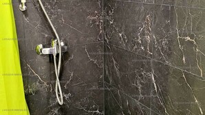 A bathroom with dark marble walls, a shower with a handheld showerhead, and a white bathtub.