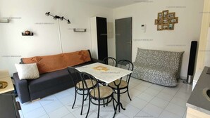 A compact living space with a sofa, a dining table with chairs, a coffee table, a black door, and a wall with framed pictures.