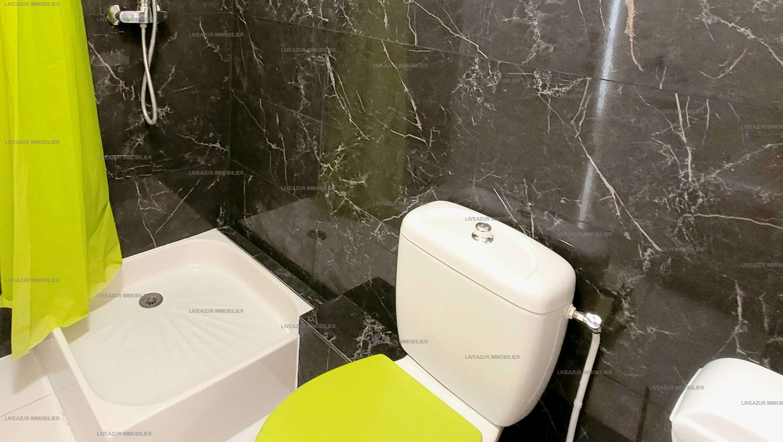A bathroom with a white toilet, a green shower curtain, and a marble backsplash.