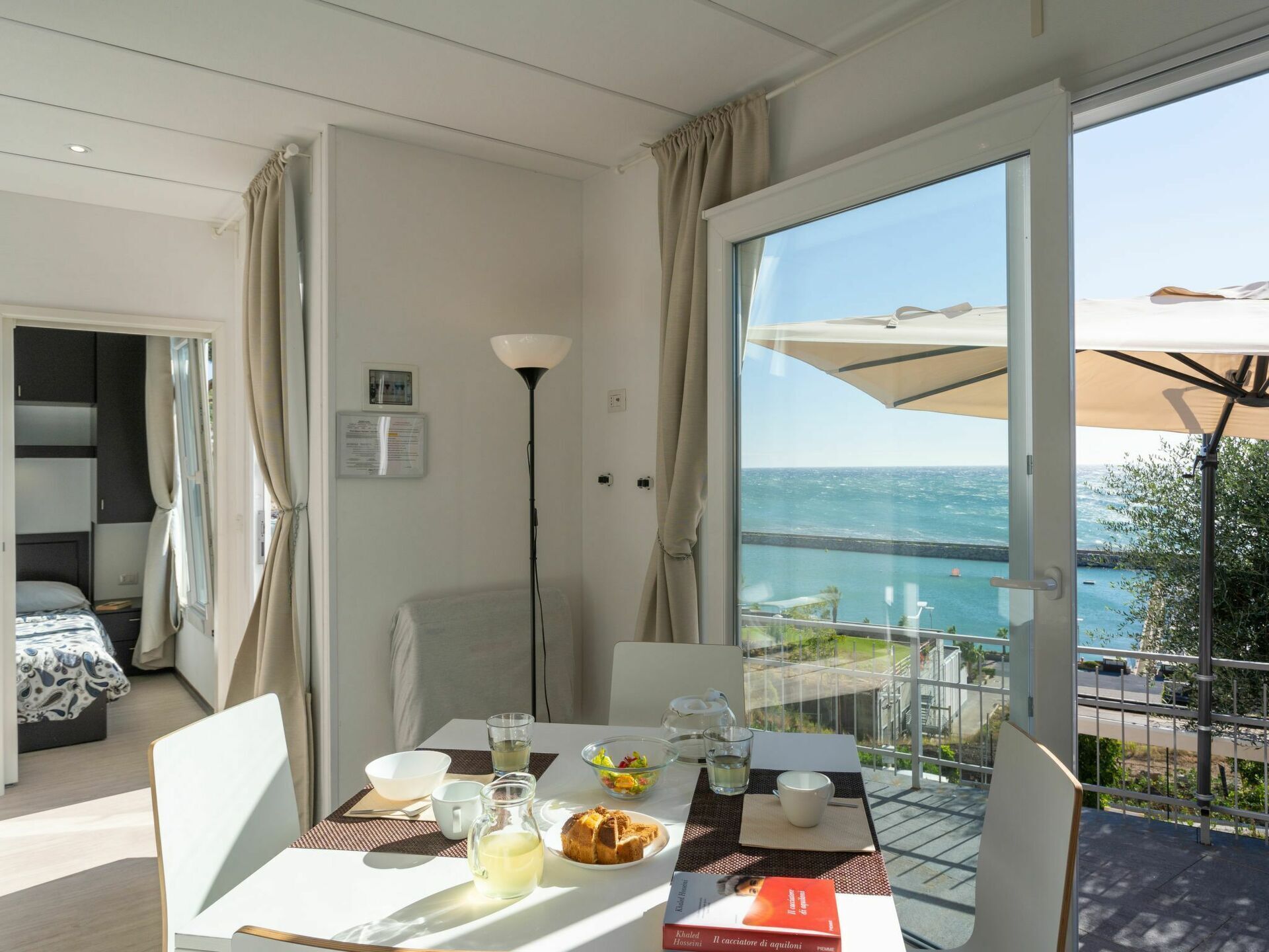 Ein Hotelzimmer mit Balkon und Meerblick, einem Esstisch mit Frühstücksgebäck und einem Bett mit gemustertem Überwurf.