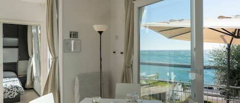 Une chambre d’hôtel avec un balcon donnant sur la mer, une table à manger avec des produits pour le petit-déjeuner et un lit recouvert d’une courtepointe à motifs.