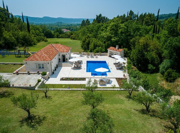 A large house with a swimming pool, surrounded by lush greenery and hills.