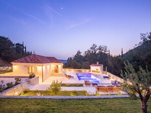 A modern villa with a swimming pool, outdoor seating, and a view of the sea.