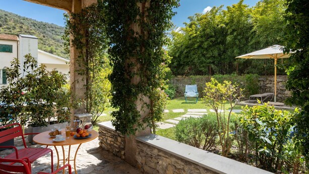 A patio with a table set for breakfast, a red chair, and a stone wall. - Nice apartment for 10 people with WIFI, TV, terrace, pets allowed and panoramic view (Dolcedo)
