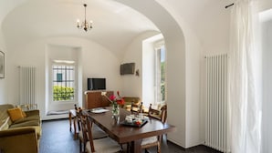 A dining area with a long table, chairs, a chandelier, and a view of greenery outside. - Nice apartment for 10 people with WIFI, TV, terrace, pets allowed and panoramic view (Dolcedo)