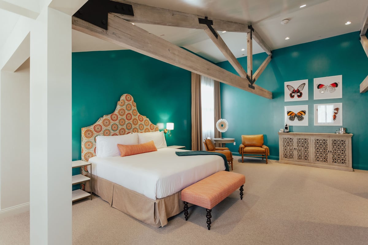A bedroom with a large bed, a wooden ceiling, teal walls, and butterfly artwork.