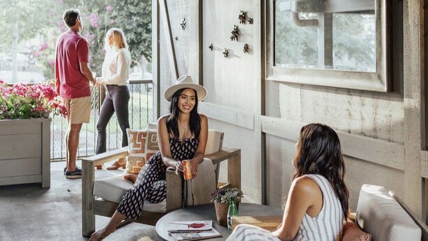 An outdoor seating area with a mix of seating options, including a sofa and a round table. There are decorative elements like wall-mounted flowers and a window with a view. - The Winston Solvang (Solvang)