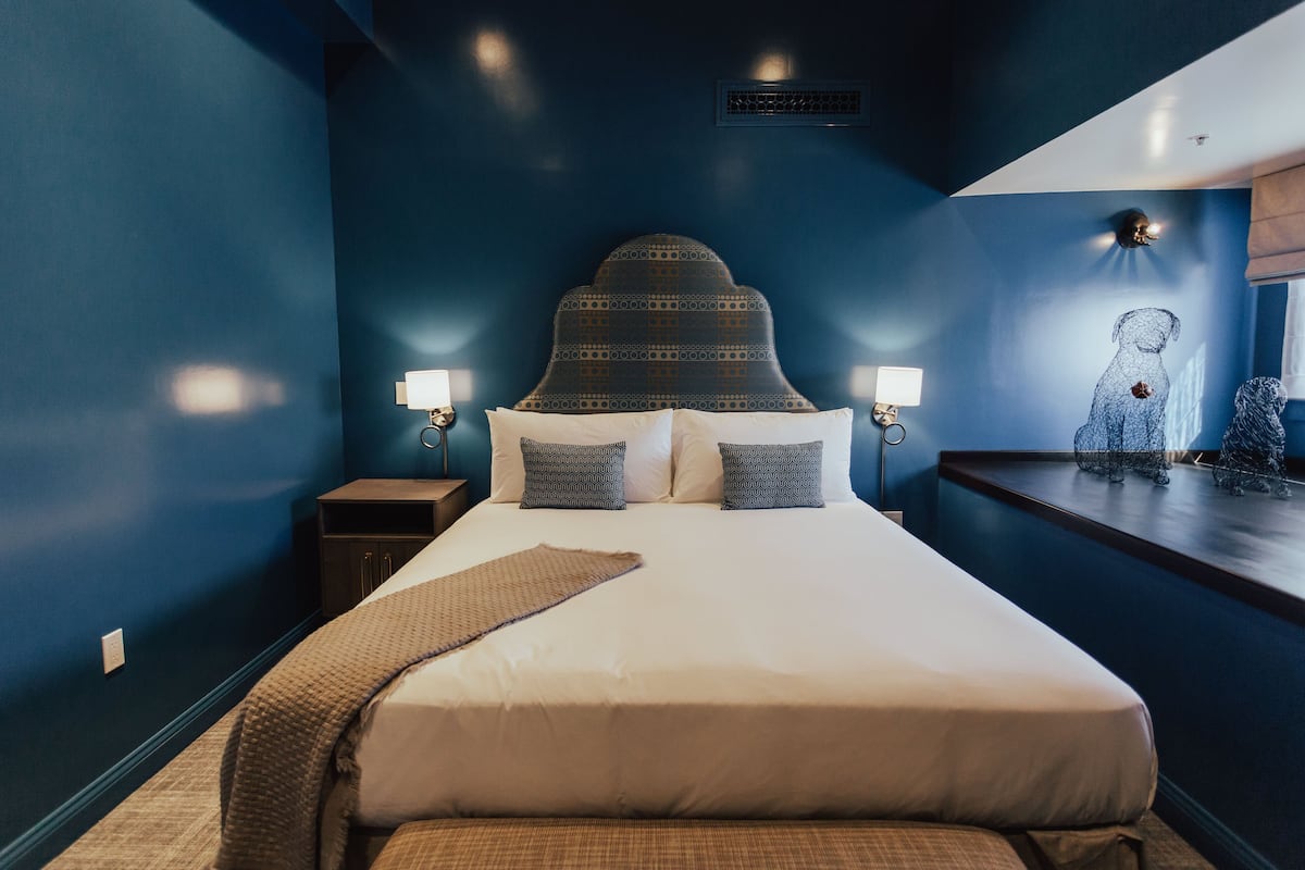 A neatly made bed with a patterned headboard, two bedside lamps, and a decorative dog sculpture on a nightstand.