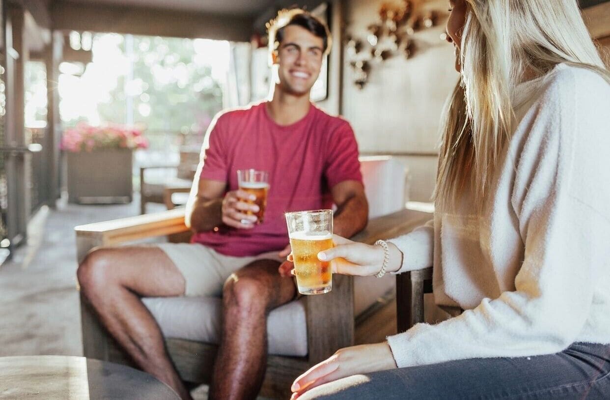 A couple sitting on a wooden bench in a cozy, sunlit outdoor seating area with a rustic decor.