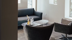 A modern interior with a dark gray sofa, a round coffee table, and a dark armchair. There are arched windows and a hanging light fixture. - The Winston Solvang (Solvang)