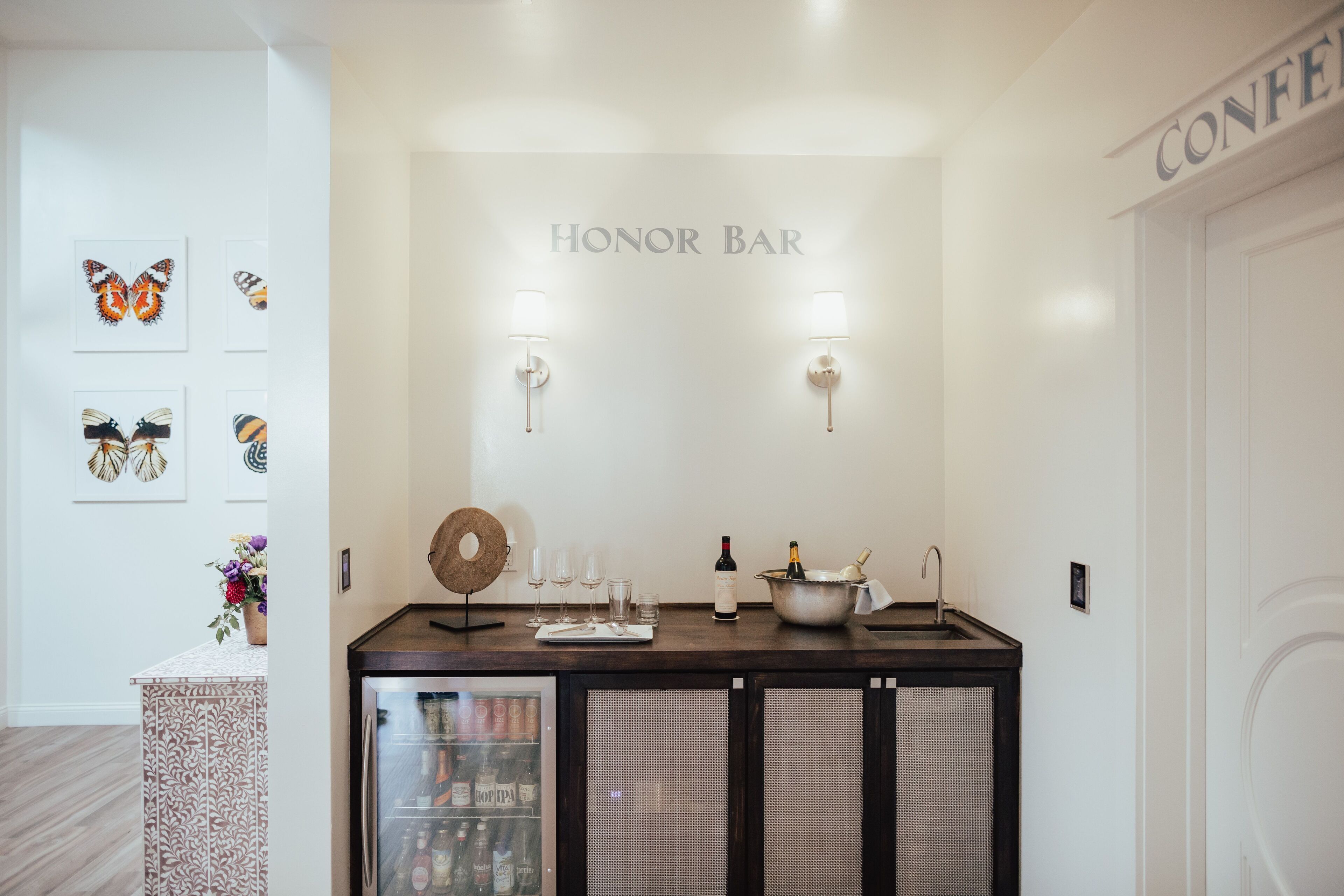 Un coin bar avec une pancarte indiquant « BAR LIBRE-SERVICE », une sélection de verres, de bouteilles et un bol décoratif.