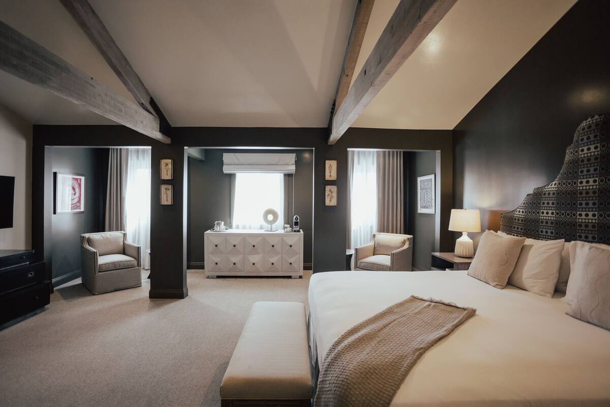 A hotel room with a large bed, two armchairs, a dresser, and a television.