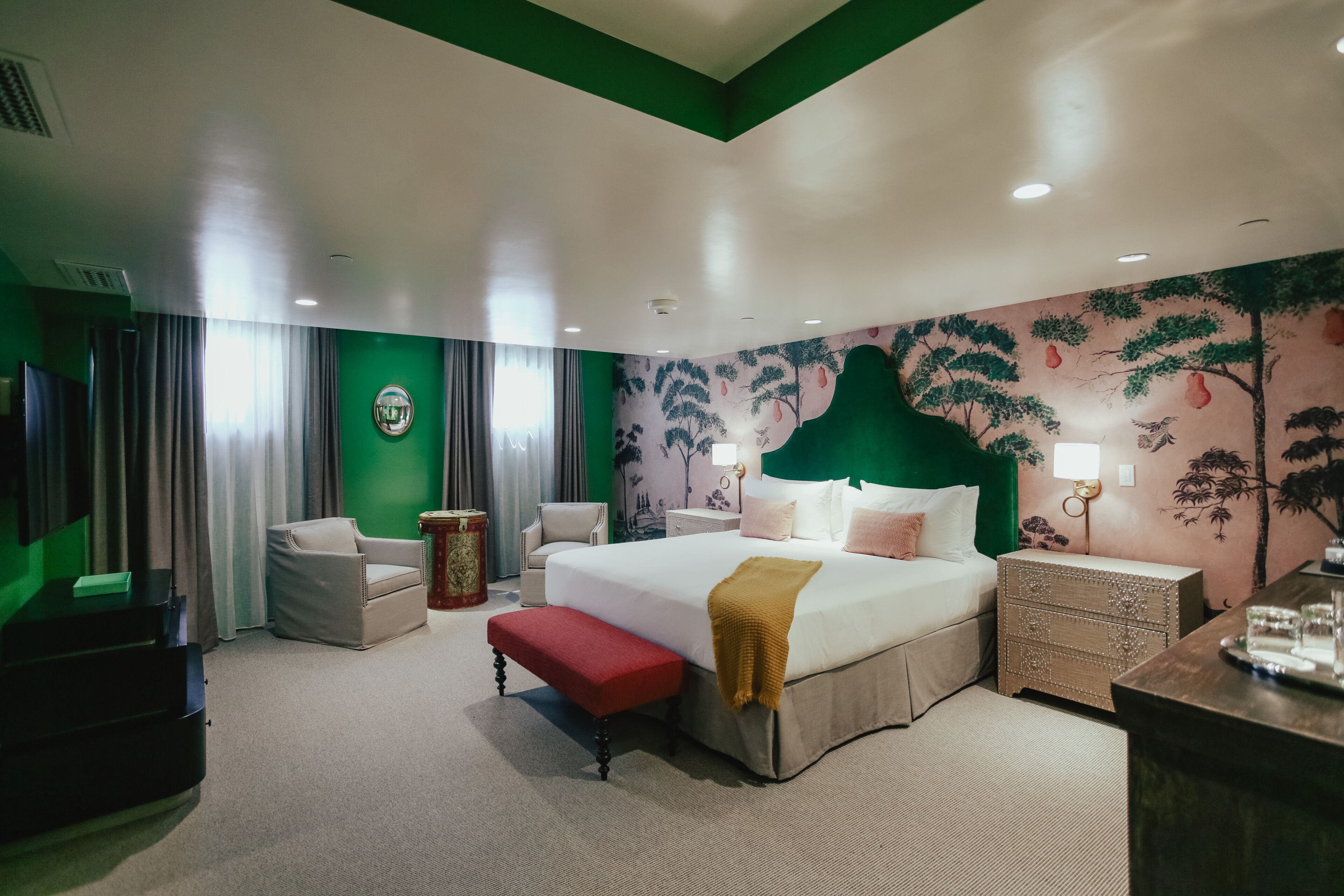 Una habitación de hotel con una cama grande, dos sillas, un banco, una mesita de noche y un aparador.