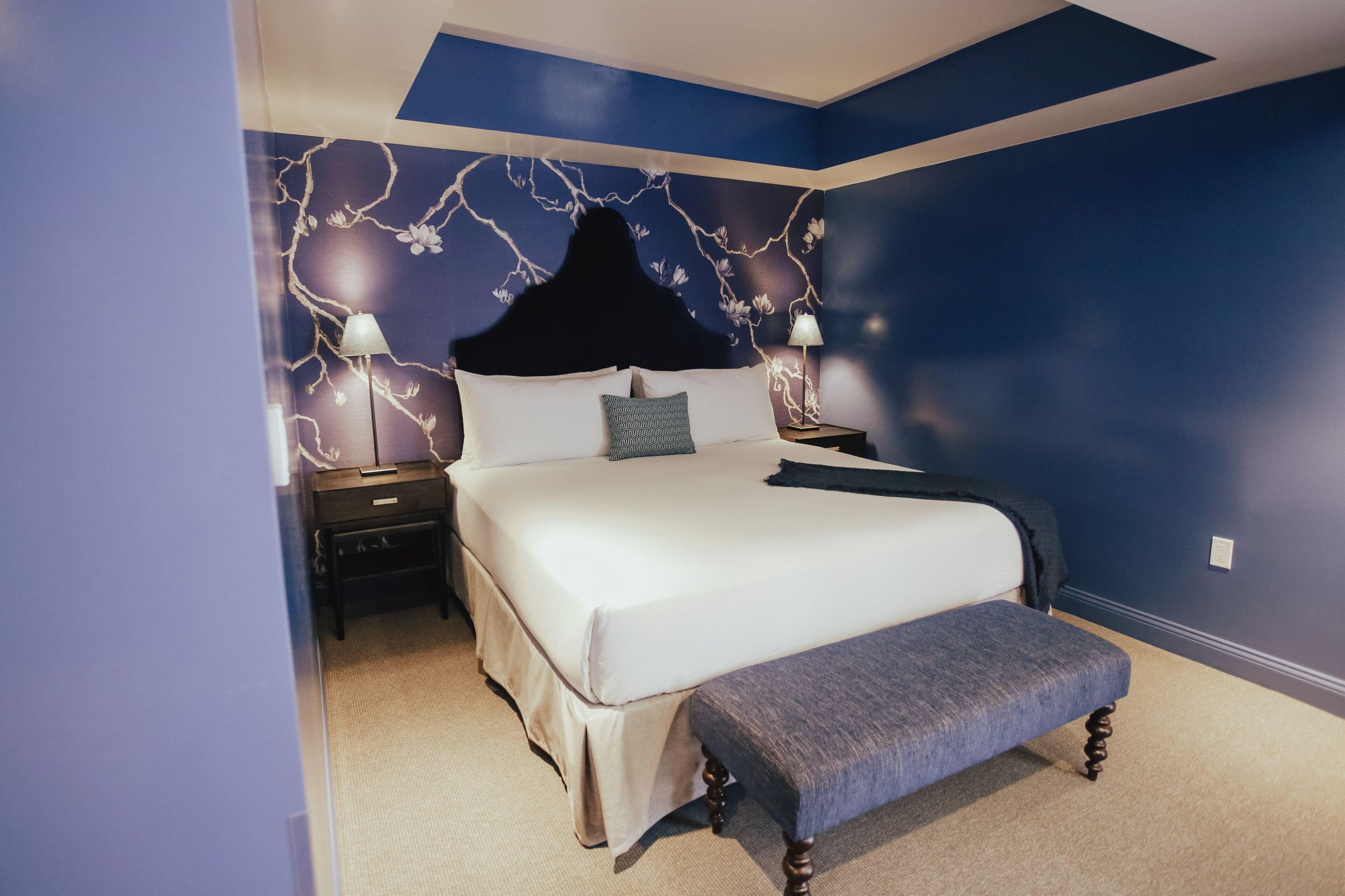 A bedroom with a large bed, two bedside tables, a bench, and a decorative headboard.
