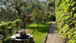 A garden with a wooden cabin, a stone bench with flowers, and a gravel path. - Nice apartment for 6 guests with WIFI, pool, TV and patio (Dolcedo)