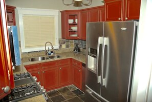 Una cocina con armarios rojos, un refrigerador de acero inoxidable, una estufa a gas y una ventana con persianas.