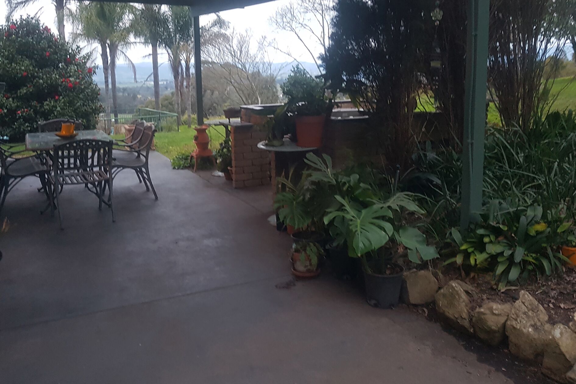 An outdoor patio area with a table and chairs, surrounded by potted plants and a brick wall.