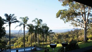 Un balcón con dos copas de vino y vistas a un paisaje exuberante con árboles y colinas lejanas.