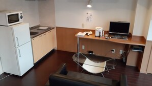 Eine kleine Küche mit Mikrowelle, Spüle und kleinem Kühlschrank. Ein Holztisch bietet Platz für eine Kaffeemaschine, einen Laptop und einen Fernseher.