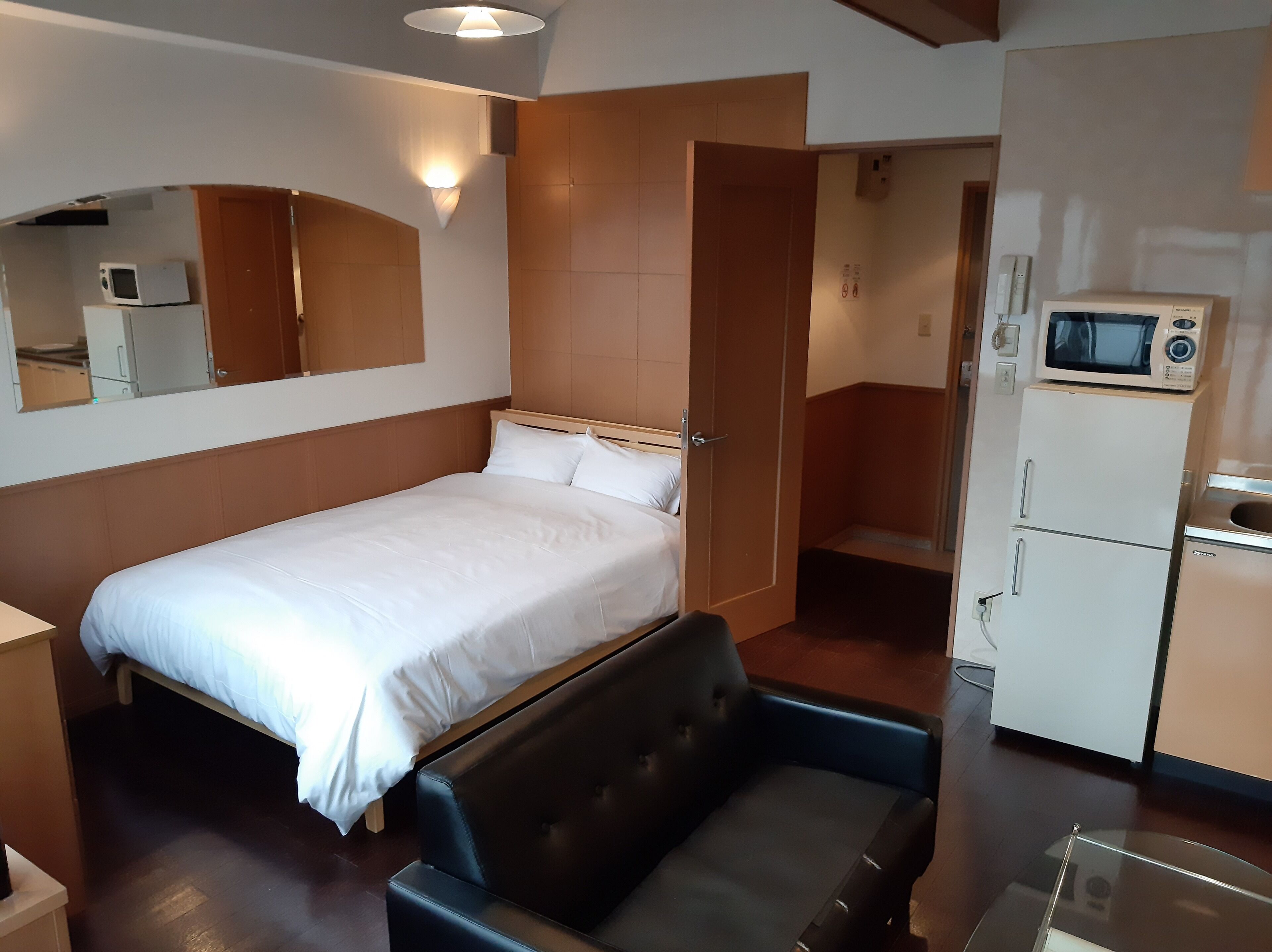 A compact hotel room with a single bed, a small seating area, a microwave, and a refrigerator.