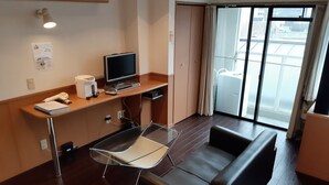 Ein Hotelzimmer mit Schreibtisch, Stuhl, Fernseher und einem großen Fenster mit Blick auf Gebäude.