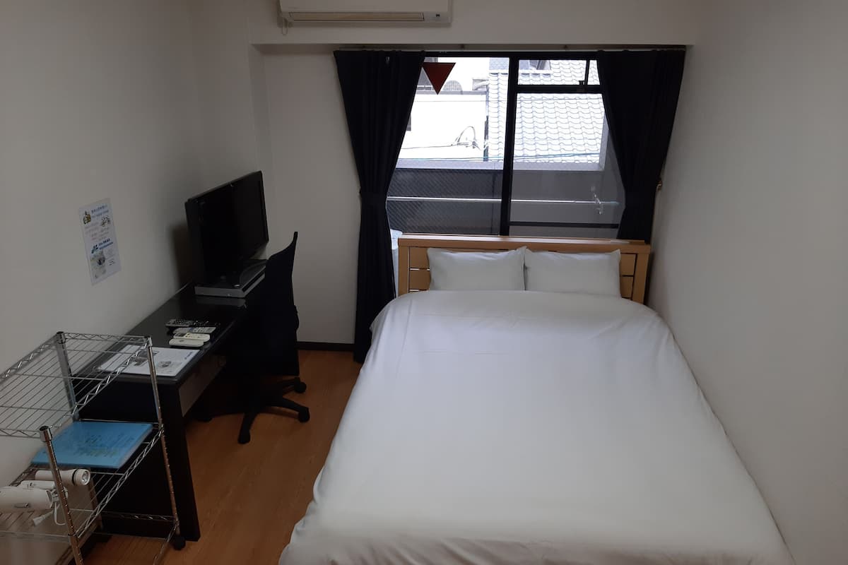 Quarto de hotel com uma cama, uma escrivaninha com computador, uma cadeira e uma televisão.