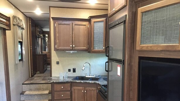A compact kitchen with wooden cabinets, a stainless steel refrigerator, a built-in oven, and a large screen TV. - Camper at the Sequoia Forest Retreat (Badger)