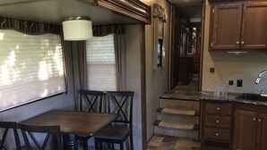 A compact kitchen with a dining area, featuring a table and chairs, a sink, and wooden cabinets. - Camper at the Sequoia Forest Retreat (Badger)