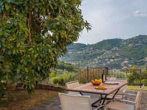 An outdoor dining area with a table set for two, surrounded by chairs, overlooking a hillside with scattered houses. - Beautiful apartment in villa for 4 guests with WIFI, TV, patio, pets allowed and panoramic view (Imperia)