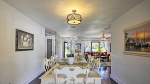 A dining room with a long table, white chairs, a chandelier, and a painting on the wall. - Pet-Friendly Oasis w/ Deck & Fire Pit in Bokeelia! (Bokeelia)