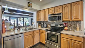 A modern kitchen with wooden cabinets, stainless steel appliances, and a large window. - Pet-Friendly Oasis w/ Deck & Fire Pit in Bokeelia! (Bokeelia)