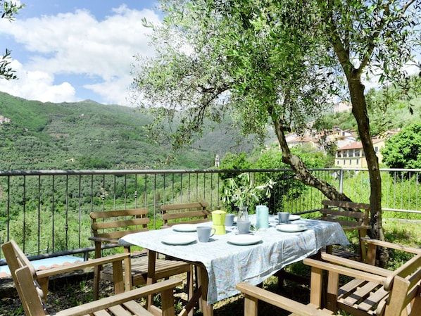 An outdoor dining area with a table set for four, surrounded by wooden chairs, overlooking a lush green valley and distant buildings.
