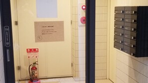 Interior de un ascensor con extintor, señal de salida de emergencia y panel de alarma contra incendios.