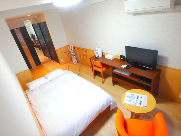 A hotel room with a bed, a desk with a television, a chair, and a small table with a menu.