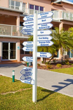 Un poste de señales direccionales con varias flechas indicando diferentes servicios, como el Centro de Actividades, la Playa y el Edificio Delfín.