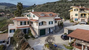A two-story house with a stone facade, a red-tiled roof, and a driveway leading to a parked car. - Beautiful apartment for 4 people with WIFI, pool, TV, patio and pets allowed (Diano Castello)