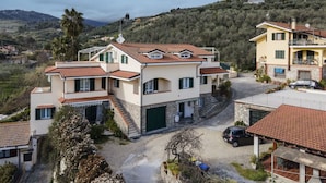 A two-story house with a stone facade, a red-tiled roof, and a driveway leading to a parked car. - Beautiful apartment for 6 guests with WIFI, pool, TV, terrace and pets allowed (Diano Castello)