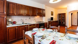 Une cuisine avec des meubles de rangement en bois, une table à manger dressée pour quatre personnes et un luminaire suspendu.