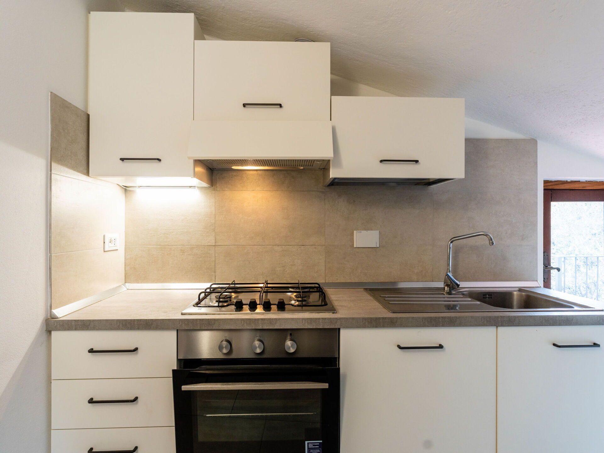 A modern kitchen with white cabinets, a gas stove, an oven, and a stainless steel sink.