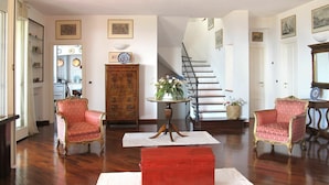 Un vaste salon doté de parquet, de deux fauteuils rouges élégants, d’une commode en bois et d’un escalier menant à un autre niveau.