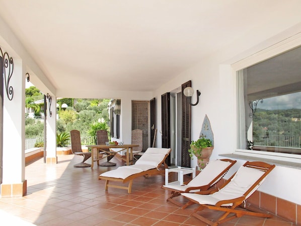 A sunlit patio with two wooden lounge chairs, a small table, and a potted plant.