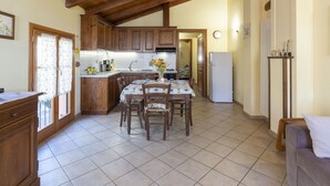 A kitchen with wooden cabinets, a tiled floor, a dining table with chairs, a refrigerator, and a clock on the wall. - Lovely apartment for 4 people with WIFI, TV, patio, pets allowed and panoramic view (Vendone)