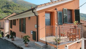 A two-story house with a balcony, potted plants, and a view of the surrounding hills. - Lovely apartment for 4 people with WIFI, TV, patio, pets allowed and panoramic view (Vendone)