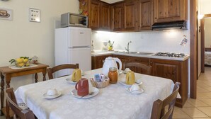 Una cucina con mobili in legno, un frigorifero bianco, un forno a microonde, un lavello e un tavolo da pranzo apparecchiato con tazze e un boccale.
