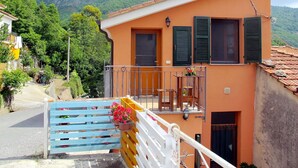 Un edificio a due piani con un balcone, un cancello in legno e montagne sullo sfondo.